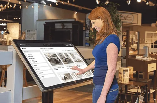 Woman interacting with a large touchscreen kiosk displaying real estate listings inside a showroom.