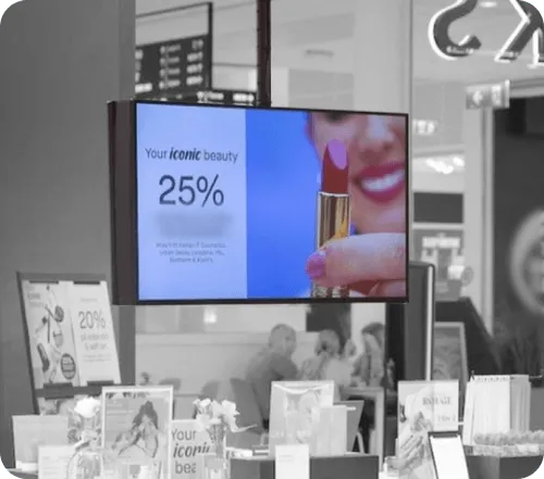 Retail display with a screen showing a lipstick and text offering 25% off on iconic beauty products.