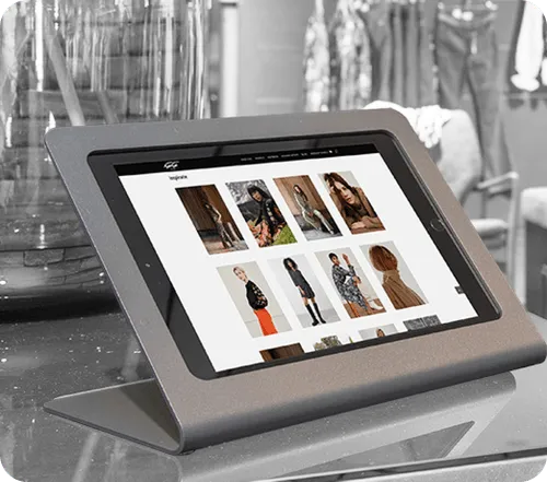Tablet in a gray stand displaying a fashion website with images of models wearing various outfits.