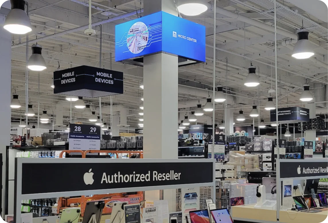 Interior of a retail electronics store with Apple Authorized Reseller signage and displays of mobile devices and laptops.